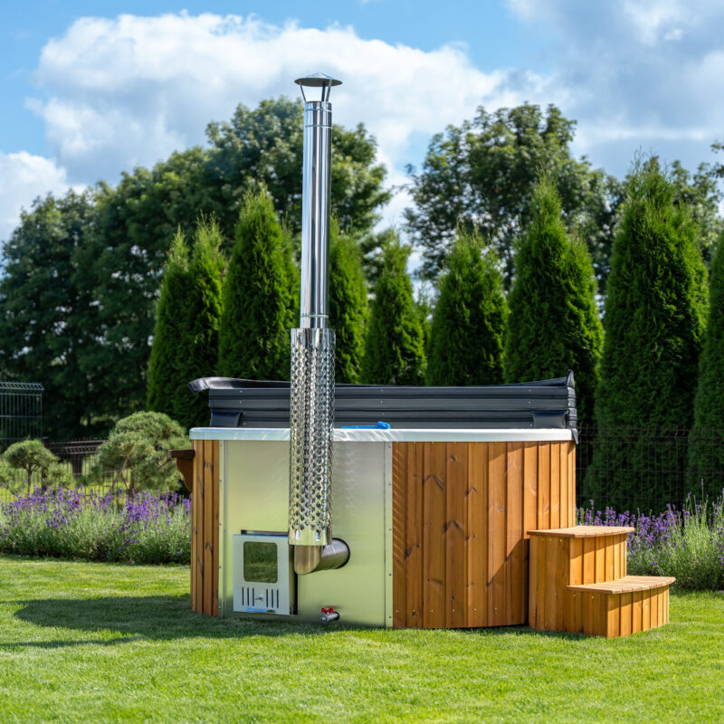Holzbefeuertes Outdoor-Badefass mit Holzverkleidung, Edelstahlschornstein und Einstiegstreppe auf einer Gartenwiese